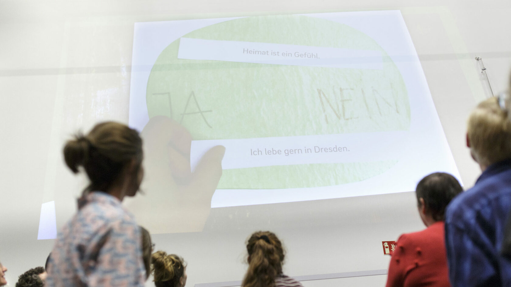 At the kick-off event for the Youth Council, young people look at a wall projection on the theme of "Heimat".