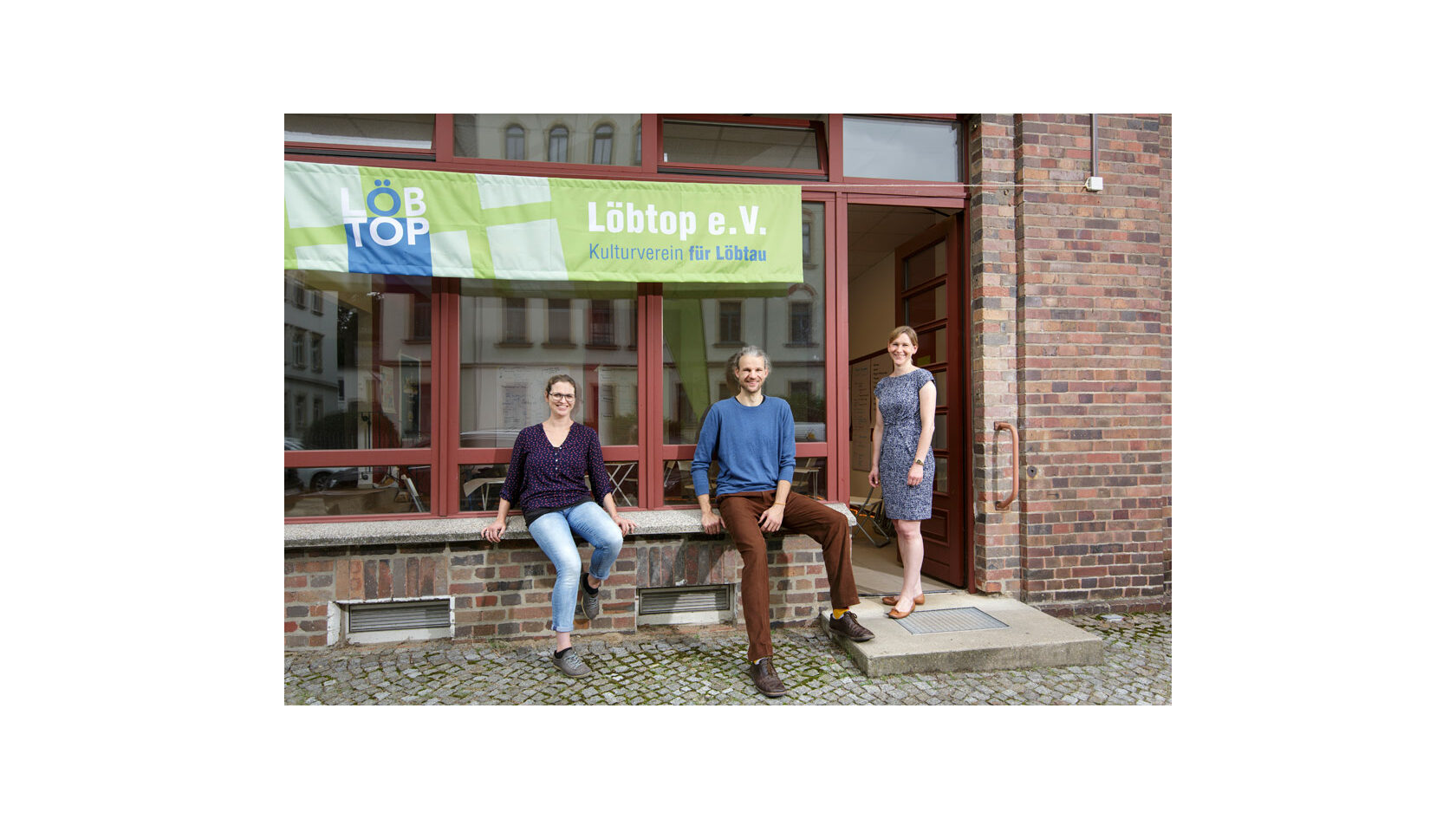 Gruppenfoto der Initiatoren des Projekts „Ideenwerkstatt 950 Jahre Löbtau“ vom Verein Löbtop e. V., Kulturverein für Löbtau. Zu sehen sind Viola Martin-Mönnich, Felix Liebig und Lina Addicks vor dem Vereinsbüro.