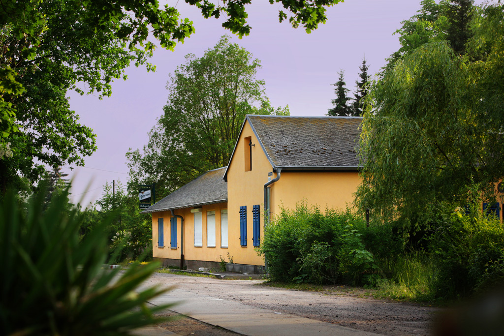 Blick auf ein gelbes Gebäude der Kleingartensparte Hellersiedlung, umgeben von Bäumen und Sträuchern