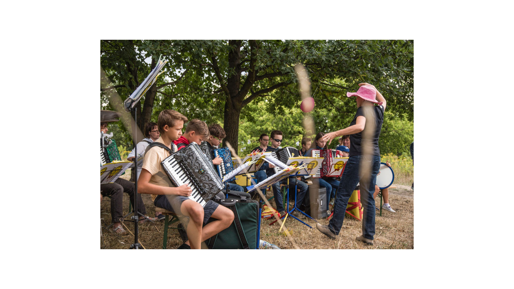 Eine Gruppe von Kindern spielt Akkordeon unter Bäumen auf dem Gelände der Hufewiesen in Trachau.