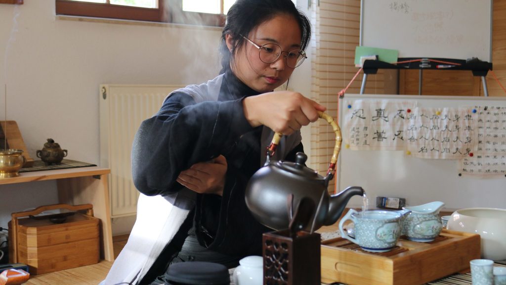 Eine junge Frau gießt während einer Teezeremonie Tee ein.