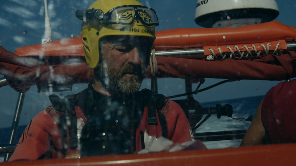Blick auf einen Mann auf einem Rettungsboot auf dem Meer mit Mission-Lifeline-Helm.