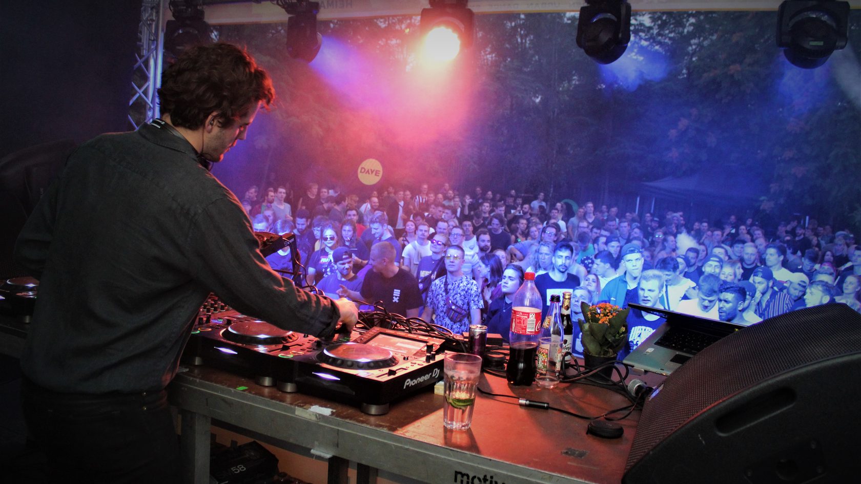 Blick auf einen DJ hinterm DJ-Pult, im Hintergrund das feiernde Publikum bei der Dresden Urban Dance Experience.