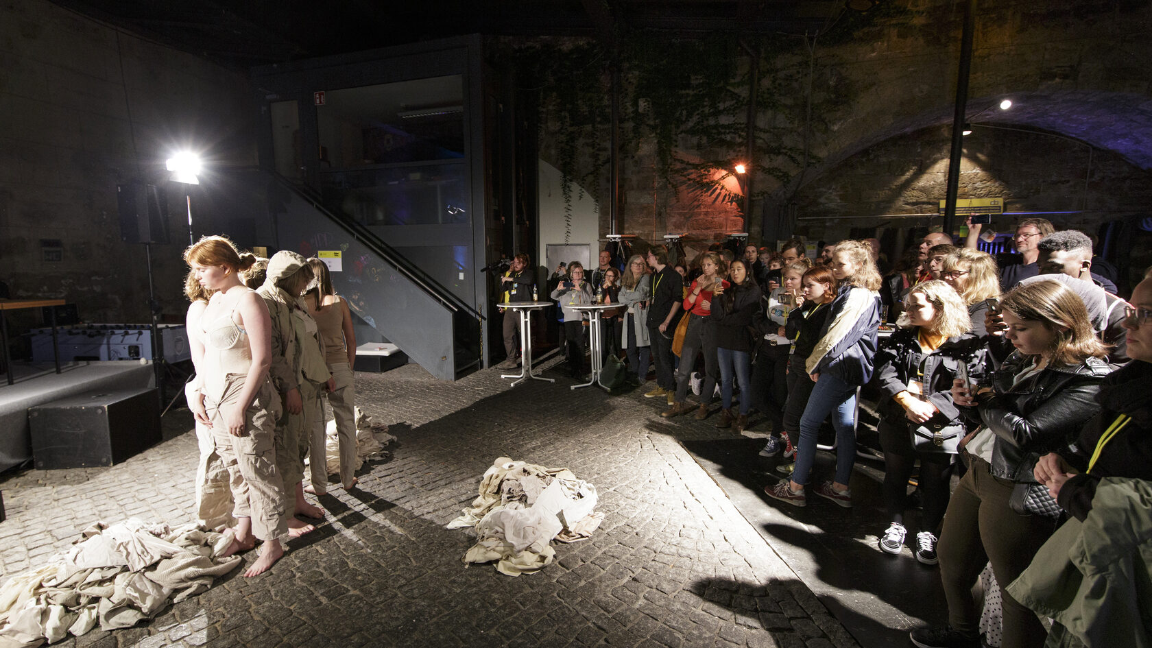 Performance of a group of young people wrapped in white clothes, standing close together while the audience watches them.