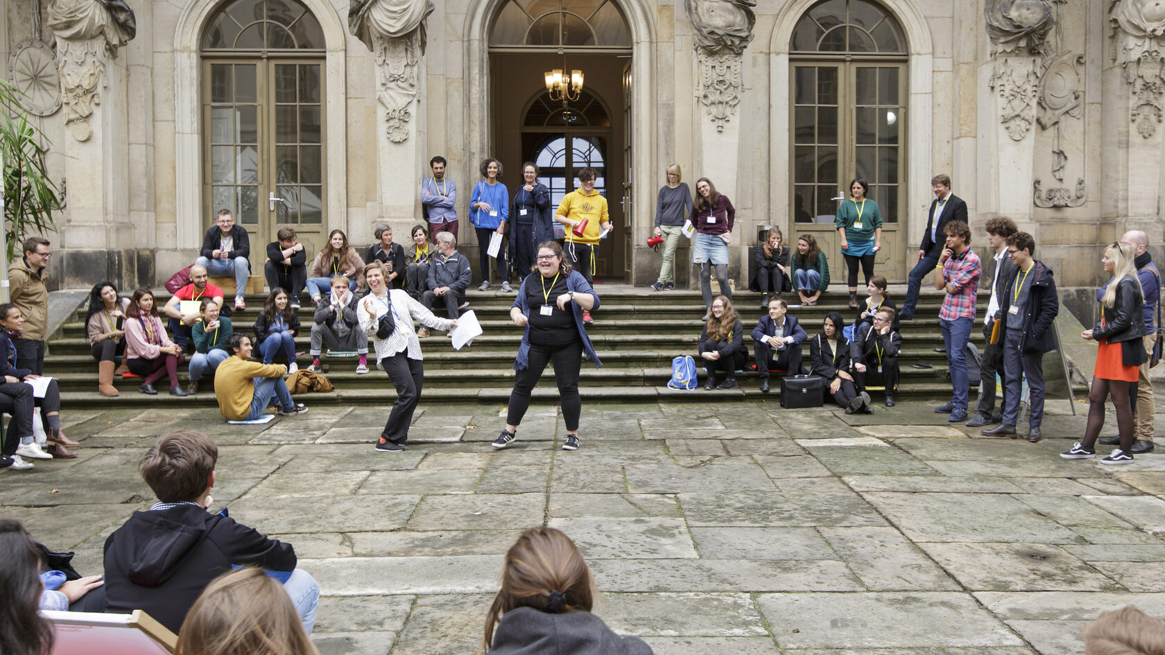 In the courtyard of the Japanese Palace, numerous young people listen to a moderator.