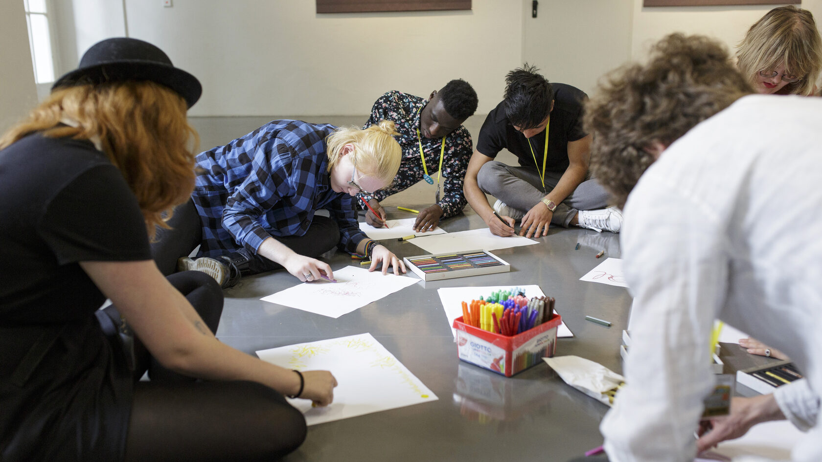 Eine Gruppe von Jugendlichen sitzt auf dem Boden und skizziert Ideen auf weiße Blätter.