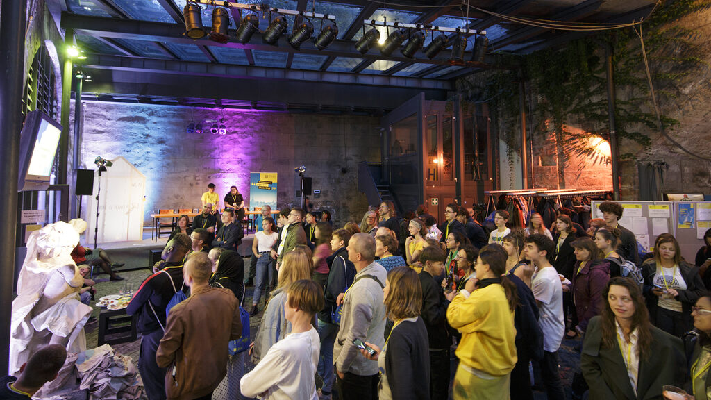 Numerous young people watch a video projection in an event room.