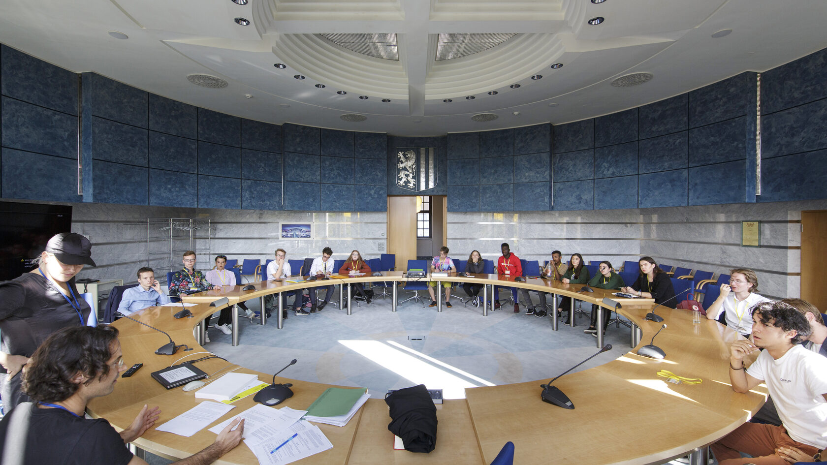 Zahlreiche Jugendliche diskutieren um einen runden Tisch versammelt in einem Tagungssaal der Landeshauptstadt Dresden.