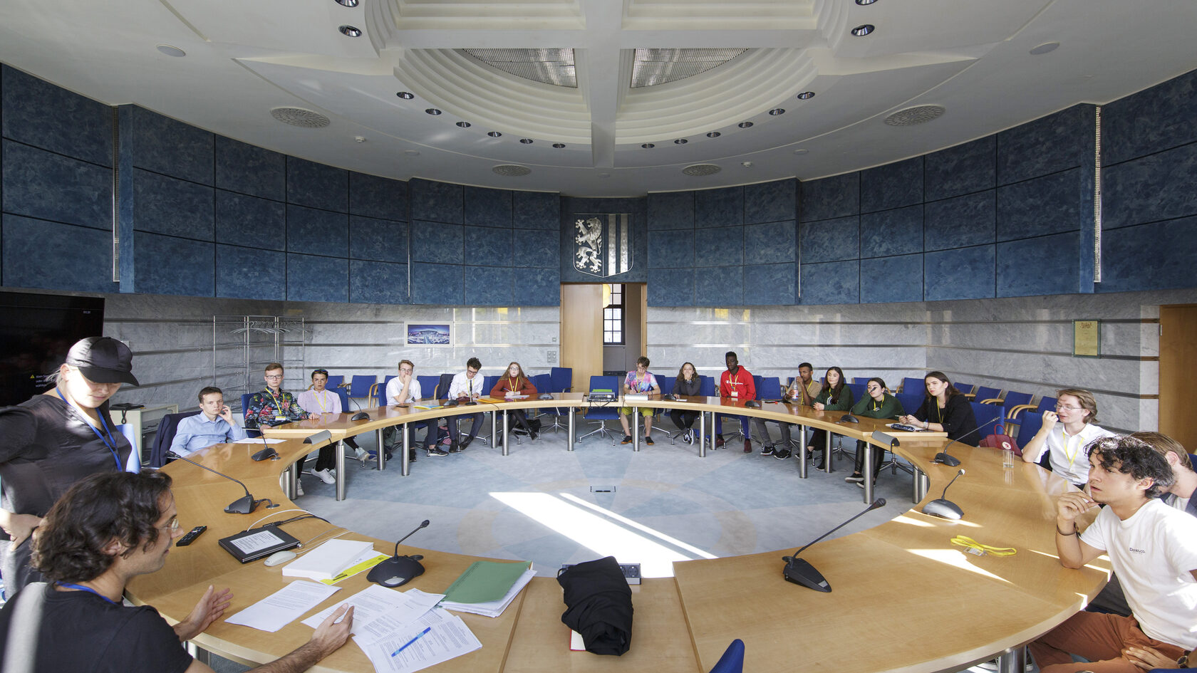 Numerous young people are gathered around a round table in a conference room in the City of Dresden.