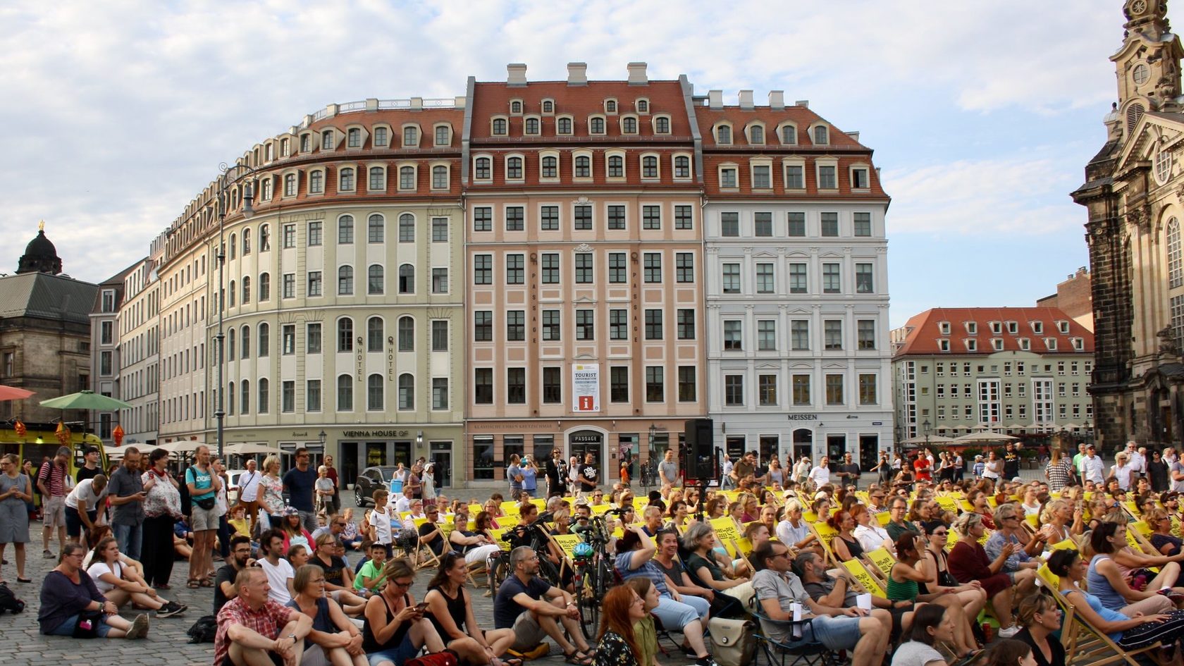 Numerous people are sitting in deck chairs on Dresden's Neumarkt square. In the background houses and a part of the Dresden Frauenkirche can be seen.